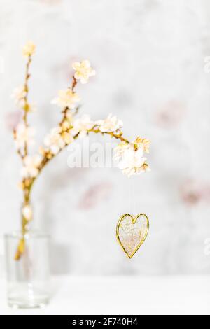 Ein goldenes Herz hängt an einem Frühlingszweig, der ist Mit Blüten bedeckt Stockfoto