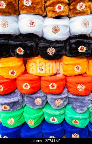 Reihen von russischen Wintermützen in verschiedenen Farben mit Armeemblemen auf dem Straßenmarkt in der Old Arbat Street in Moskau, ikonisches beliebtes Souvenir aus Russland. Hochwertige Fotos Stockfoto