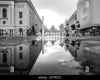 Rom, Italien - 18. August 2019: Schwarz-Weiß-Ansicht des Petersdoms in der Vatikanstadt mit Spiegelreflexion im Wasser auf der Stadtstraße. Epische Graustufen Stockfoto