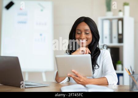 Fröhliche schwarze Geschäftsfrau mit Tablet-pc am Arbeitsplatz, im Gespräch mit Kollegen auf Webcam, Kopierraum Stockfoto