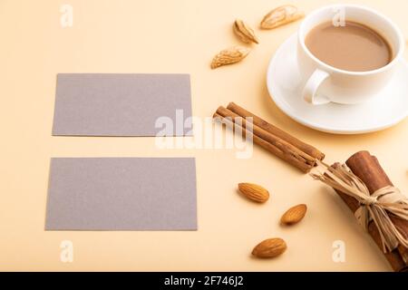 Komposition aus grauen Papier Visitenkarten, Mandeln, Zimt und Tasse Kaffee. Mockup auf orangefarbenem Hintergrund. Leer, Seitenansicht, Standzeit, Kopierbereich. Stockfoto