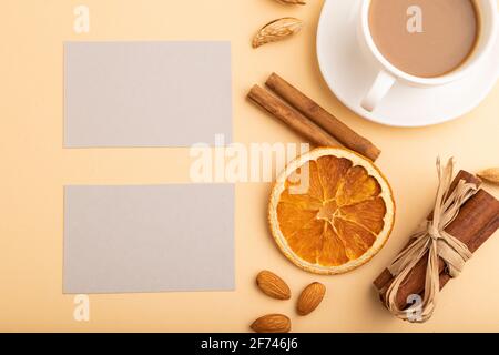 Komposition aus grauen Papier Visitenkarten, Mandeln, Zimt und Tasse Kaffee. Mockup auf orangefarbenem Hintergrund. Leer, Draufsicht, Stillleben, flach liegend, Polizist Stockfoto