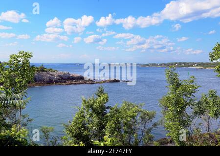 Blick auf die Bucht Danforth Cove von Fort Williams Park auf die Klippen mit Felsvorsprüngen, Baumgrenzen, geschwollene Wolken am Horizont auf den Portlandinseln Stockfoto