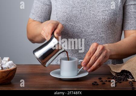 Traditioneller türkischer Kaffee in klassischen Tassen mit türkischen Köstlichkeiten. Im Hintergrund befindet sich eine Kaffeekocher aus Metall. Eine Frau gießt Kaffee in die c Stockfoto