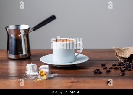 Traditioneller türkischer Kaffee in klassischen Tassen mit türkischen Köstlichkeiten. Im Hintergrund befindet sich eine Kaffeekocher aus Metall. Stockfoto