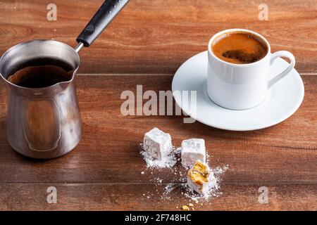 Traditioneller türkischer Kaffee in klassischen Tassen mit türkischen Köstlichkeiten. Im Hintergrund befindet sich eine Kaffeekocher aus Metall. Stockfoto