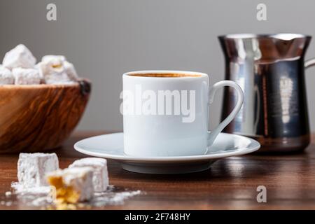 Traditioneller türkischer Kaffee in klassischen Tassen mit türkischen Köstlichkeiten. Im Hintergrund befindet sich eine Kaffeekocher aus Metall. Stockfoto