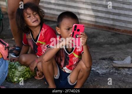Ein kleines Kind in einer armen Gegend von Cebu City auf den Philippinen, das ein Mobiltelefon benutzt, während ein junges Mädchen aufschaut Stockfoto