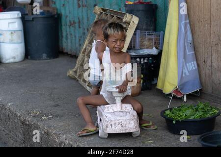 Ein kleines Kind spielt mit einer Fahrt auf Plastikspielzeug in einer armen Gegend von Cebu City auf den Philippinen. Stockfoto