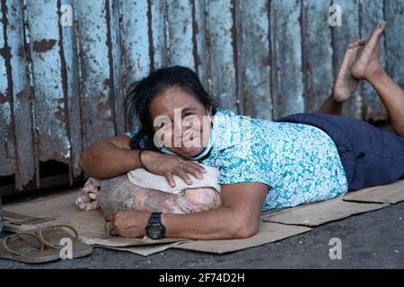 Eine obdachlose philippinische Frau lächelt auf die Kamera zu, während sie lügt Auf der Seitenstraße auf Pappe, wo sie schläft Stockfoto