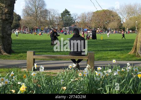 Am ersten Wochenende nach dem ersten Schritt aus dem Lockdown saß ein Mann auf einer Bank und geniesst das warme Frühlingswetter inmitten von Menschengruppen im Central Park in Newham. Am 29. März wurde die ‘Stay Home’-Anordnung aufgehoben, die es den Menschen erlaubte, sich entweder in Gruppen von sechs Personen oder als zwei Haushalte im Freien zu treffen. Boris Johnson wird das Land am Montag über die nächsten Schritte aus dem Lockdown informieren, ob England in die nächste Phase der Wiedereröffnung übergehen kann. Stockfoto