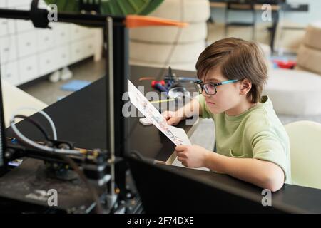 Hochwinkelporträt eines kleinen Jungen mit 3D-Drucker während des Engineering- und Robotikunterricht an der modernen Schule, Kopierraum Stockfoto