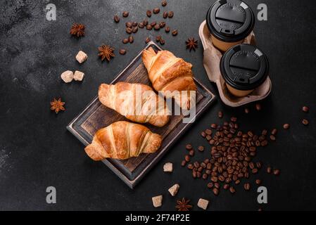 Frisches, leckeres französisches Croissant mit einer Tasse duftendem Kaffee auf dunklem Beton. Stärkendes Frühstück Stockfoto