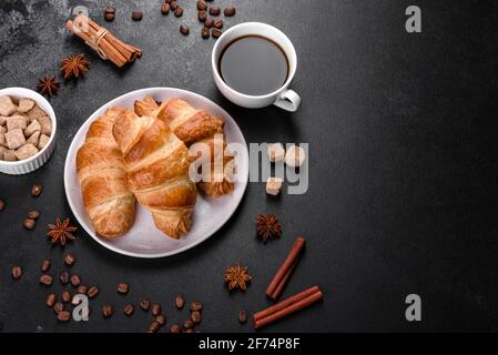 Frisches, leckeres französisches Croissant mit einer Tasse duftendem Kaffee auf dunklem Beton. Stärkendes Frühstück Stockfoto