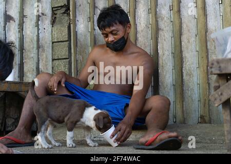 Ein philippinischer Mann füttert einen Welpen aus einer Tasse auf einem Bürgersteig in einer armen Gegend von Cebu City, Philippinen Stockfoto