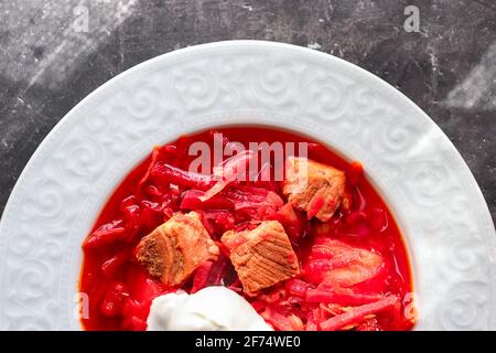 Roter Borsch mit Gemüse und Fleisch auf einem weißen Teller. Tomatensuppe. Dunkler Hintergrund. Leckeres, gesundes Mittagessen. Nahaufnahme Stockfoto