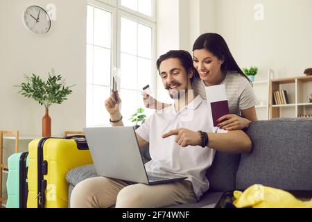 Glückliches Ehepaar zu Hause, das mit einem Laptop für Tickets bezahlt und online ein Hotelzimmer bucht. Stockfoto