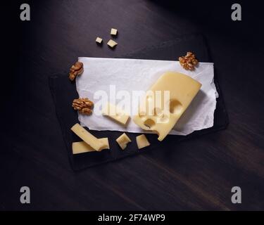 Hartkäse mit Löchern in Stücken und in Scheiben und Walnüsse auf dunklem Hintergrund geschnitten. Speicherplatz kopieren. Stockfoto