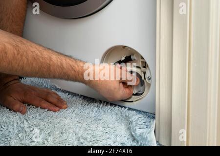 Der Master öffnet den Filter der Waschmaschine, um die Verstopfung zu beseitigen. Problem mit dem Wäschewaschen. Stockfoto