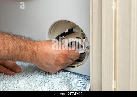 Der Mann öffnet den Filter der Waschmaschine Entfernen Sie die Unterbrechung Stockfoto