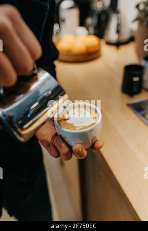 Von oben der Ernte anonymen Barista gießt Milch in den Becher Von Kaffee während der Herstellung von Latte Art in der Cafeteria Stockfoto