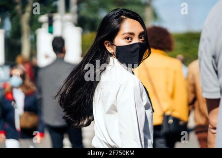 Rückansicht der asiatischen Frau mit fliegenden Haaren, die schützend tragen Maske, die in Menschenmenge läuft und die Kamera anschaut Stockfoto
