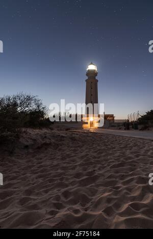 Leuchtturm mit hellen Lichtern am Sandstrand in Faro De Trafalgar in Cádáz in Spanien unter Nachthimmel mit Sterne Stockfoto