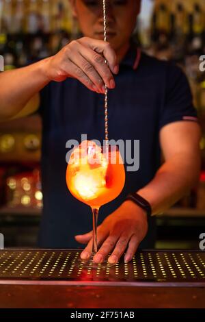 Junger asiatischer Barkeeper hält das Glas und rührt Grapefruitsaft gin-Cocktail in der Bar Stockfoto