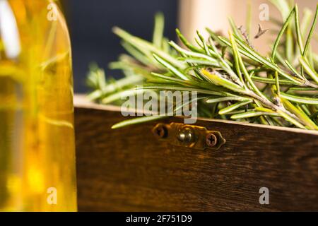 Rosmarinzweige mit grünen Blättern in einer kleinen Holzkiste In der Nähe Glasflasche mit Öl auf der Oberfläche an einem hellen Ort Stockfoto