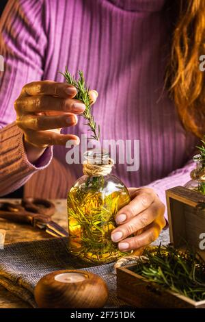 Crop gesichtslose Frau in lila Pullover setzen Kräuter Zweige mit Grüne Blätter in ätherisches Öl Glasflasche neben Schere und Seil mit kleiner Brust an Stockfoto