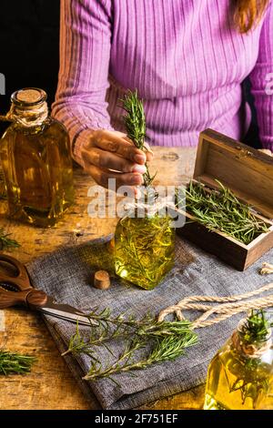 Crop gesichtslose Frau in lila Pullover setzen Kräuter Zweige mit Grüne Blätter in ätherisches Öl Glasflasche neben Schere und Seil mit kleiner Brust an Stockfoto