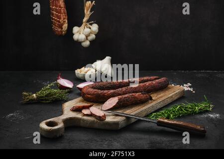 Geräucherte Schweinewurst mit Gewürzen auf Holzschneidebrett Stockfoto