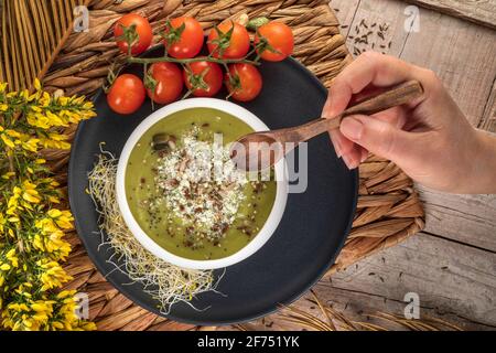 Blick von oben auf den anonymen Koch mit einer Schüssel lecker Vegetarische Sahnesuppe mit zerdrückten Pistazien und Gewürzen darauf Stockfoto