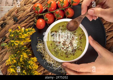 Blick von oben auf den anonymen Koch mit einer Schüssel lecker Vegetarische Sahnesuppe mit zerdrückten Pistazien und Gewürzen darauf Stockfoto