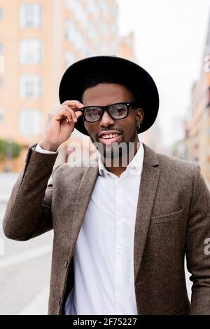 Inhalt African American männlich in stilvoller Jacke und Hut Anpassung Brille und Blick auf die Kamera, während Sie auf der Stadtstraße stehen Stockfoto