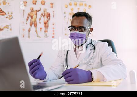 Unkenntlich schwerer schwarzer Wissenschaftler in medizinischer Robe und Maske Vorführung der Blutprobe im Reagenzglas während eines Videoanrufs Auf einem Laptop in clin Stockfoto
