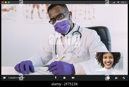 Konzentrierter afroamerikanischer Arzt in medizinischer Robe und Maske Blick auf die Kamera, während sie während des Videos mit einer positiven Frau kommuniziert Anrufen Stockfoto