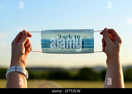 Weibliche Hände halten eine medizinische Schutzmaske mit dem Text „Back to School“. Covid-19-Pandemiethema. Stockfoto