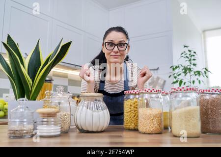 Lagern von Lebensmitteln in der Küche, Frau mit Gläsern und Behältern reden und Blick auf die Kamera Stockfoto