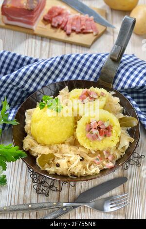 Kartoffelknödel gefüllt mit Südtiroler Speck und serviert mit Sauerkraut in einer eisernen Pfanne Stockfoto