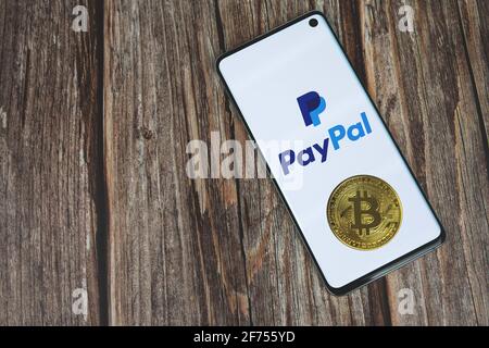 PayPal-Logo auf Telefonbildschirm mit Bitcoin Kryptowährung Münze auf Holzhintergrund mit Kopierraum. Kasse mit Crypto-Konzept Stockfoto