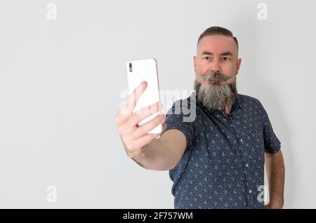 Bärtiger Hipster-Stil mit kaukasischem Aussehen 40-45 Jahre alt mit dem Smartphone, um ein Selbstporträt zu machen, Selfie. Selektiver Fokus Stockfoto