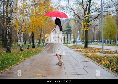 Frau im Park, die unter einem roten Schirm tanzt Der Herbstregen Stockfoto