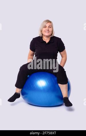 Reife Frau macht Yoga zu Hause auf einem blauen Ball. Er verbringt seine Zeit zu Hause. Stockfoto