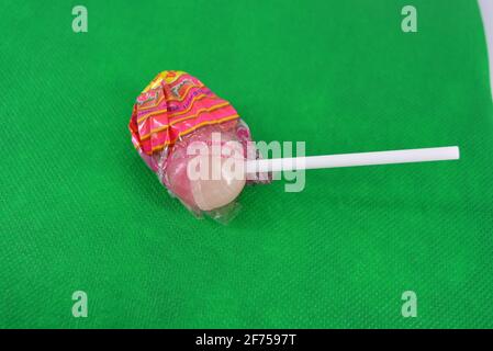 Köstliche runde süße Süßigkeiten, weiß rosa Lollipop auf weißem Kunststoff Zauberstab auf grünem Stoff Hintergrund befindet. Stockfoto