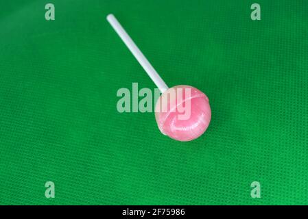 Köstliche runde süße Süßigkeiten, weiß rosa Lollipop auf weißem Kunststoff Zauberstab auf grünem Stoff Hintergrund befindet. Stockfoto