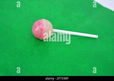 Köstliche runde süße Süßigkeiten, weiß rosa Lollipop auf weißem Kunststoff Zauberstab auf grünem Stoff Hintergrund befindet. Stockfoto