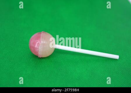 Köstliche runde süße Süßigkeiten, weiß rosa Lollipop auf weißem Kunststoff Zauberstab auf grünem Stoff Hintergrund befindet. Stockfoto