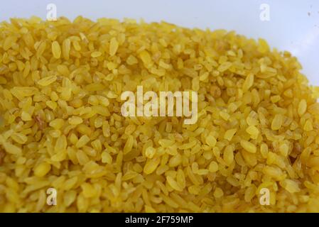 Frische Körner, Getreide, gelbe Bulgur, verstreut in Kunststoffbehälter und weißer Hintergrund mit interessanter Beleuchtung. Stockfoto
