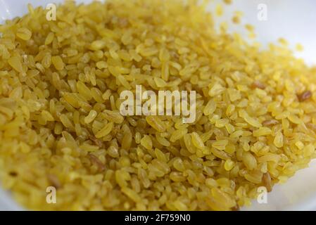 Frische Körner, Getreide, gelbe Bulgur, verstreut in Kunststoffbehälter und weißer Hintergrund mit interessanter Beleuchtung. Stockfoto